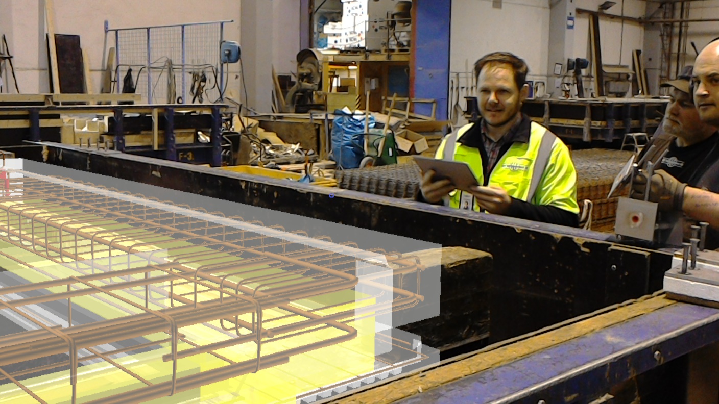 En gjutform i en betongelementfabrik. En armeringskorg ligger som hologram i formen medan en man med surfplatta står bakom.