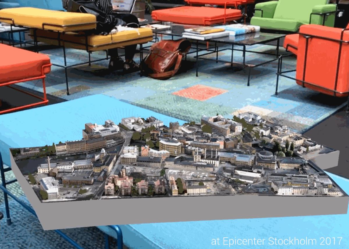 En fotogrammetrisk stadsmodell av ett kvarter ligger som hologram på ett bord i ett kontorslandskap med färgglada möbler.